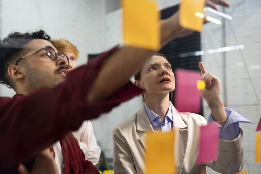 Mautic use by verticals 1 Photo of a diverse group of people looking at sticky notes on a glass wall.