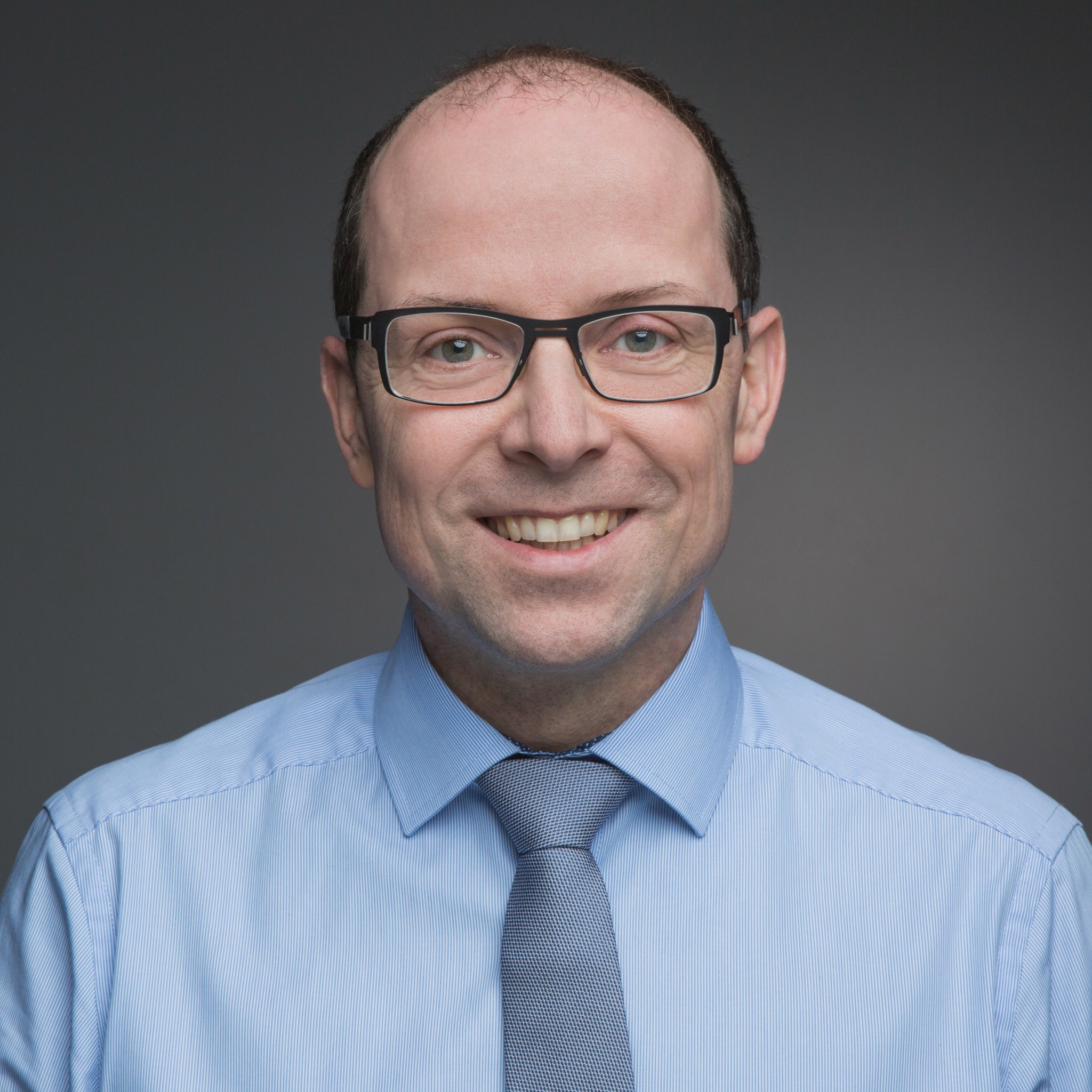 Mautic use by verticals 15 Photo of a white man looking at the camera. He's wearing glasses and has a bald head. He's wearing a pale blue shirt and a darker grey tie.