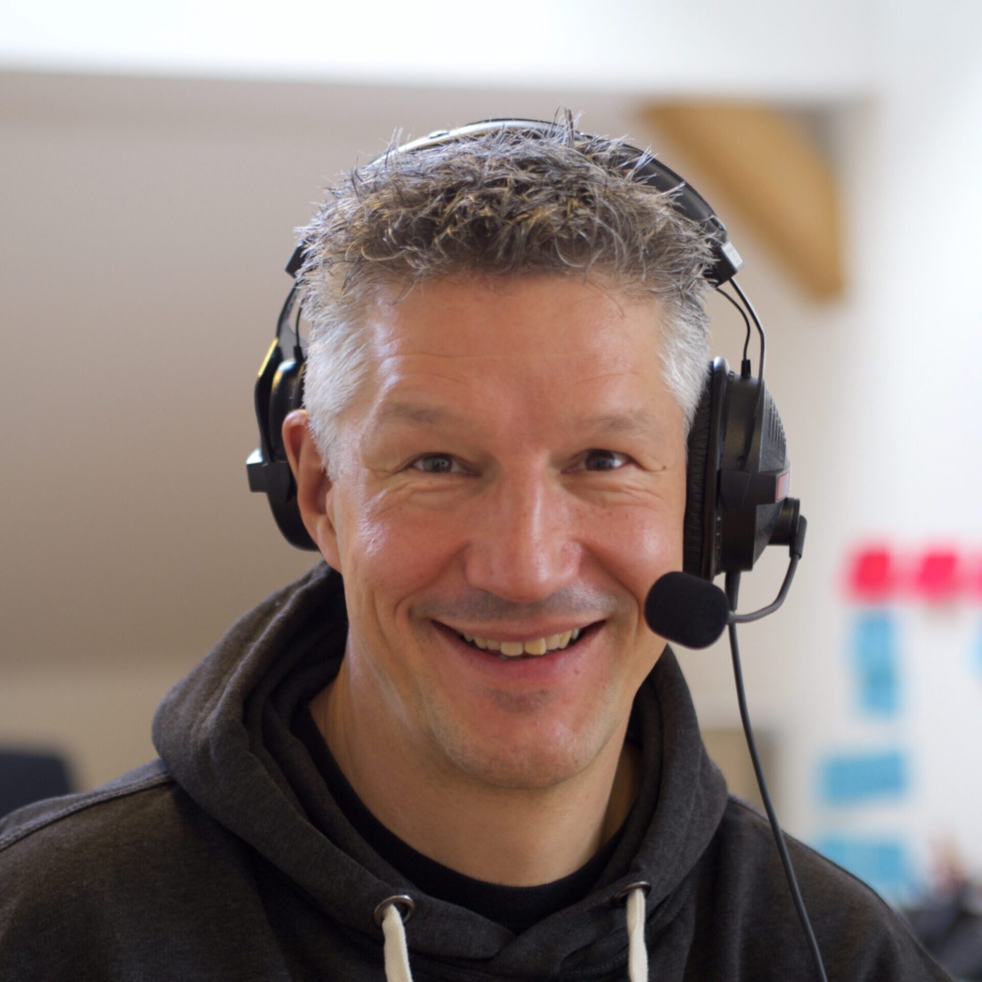 Become a member of Mautic 6 Photo of a German man wearing a headset with the microphone near his mouth. He has short, spikey grey hair and is wearing a dark coloured hoodie with white strings.
