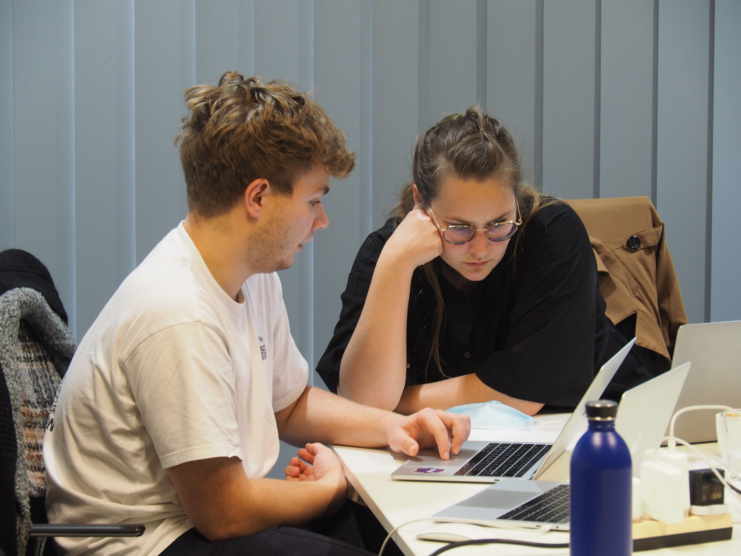 Slack 1 Photo of two people sitting at a desk, a man and a woman, looking at a laptop.