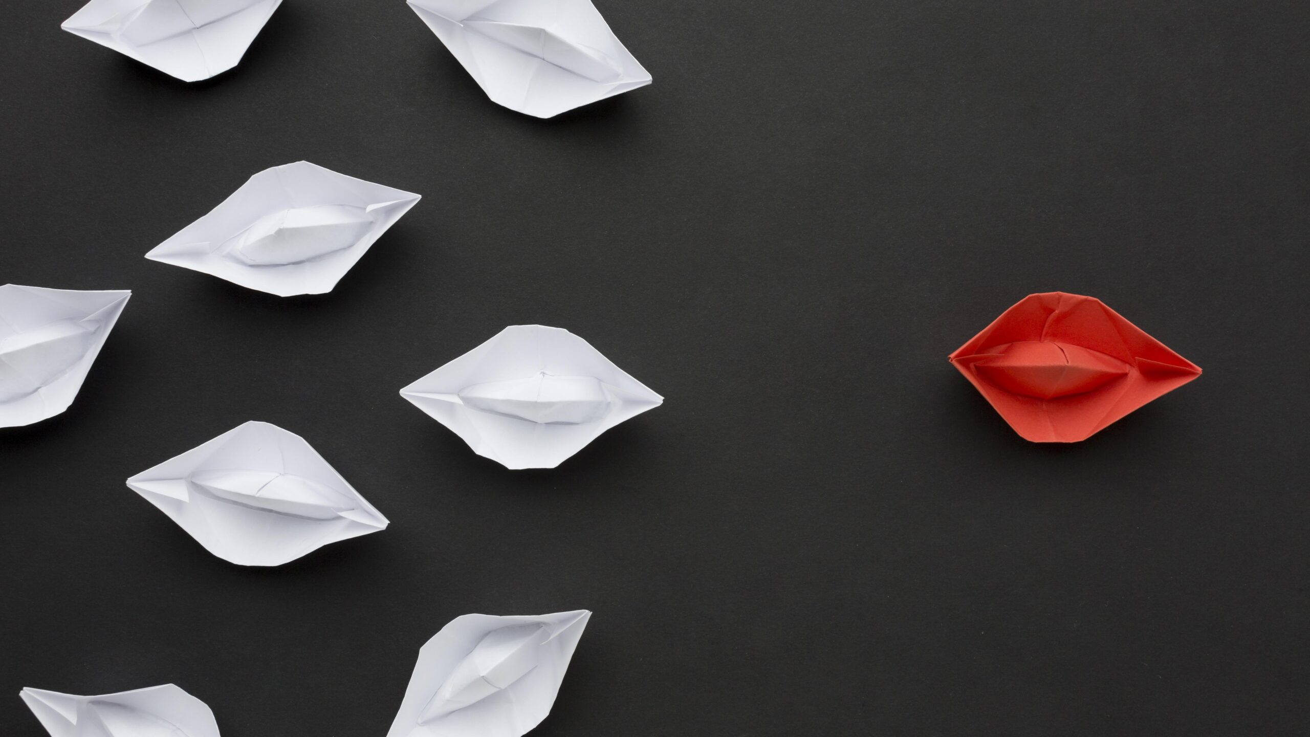 Governance 3 Image of a red origami boat in front of multiple white origami boats on a black background.